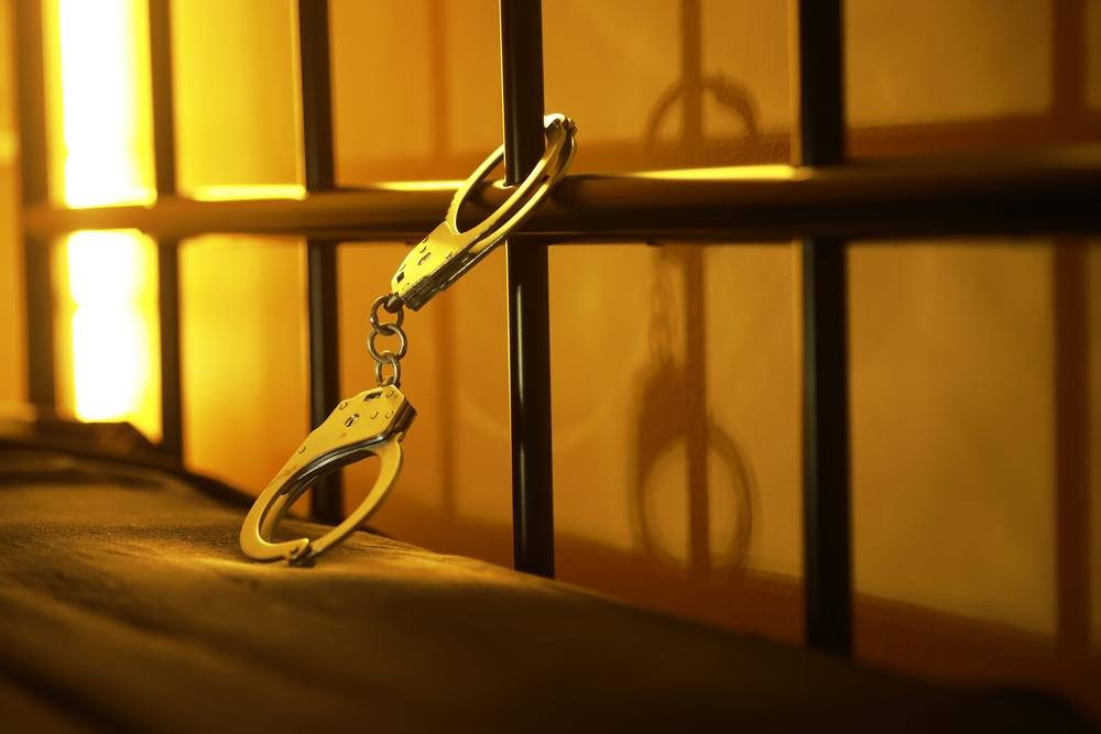 A pair of handcuffs hangs in front of jail cell bars. Rape in Ohio carries multiple penalties, including prison time, mandatory sex offender registration, and a permanent felony record.