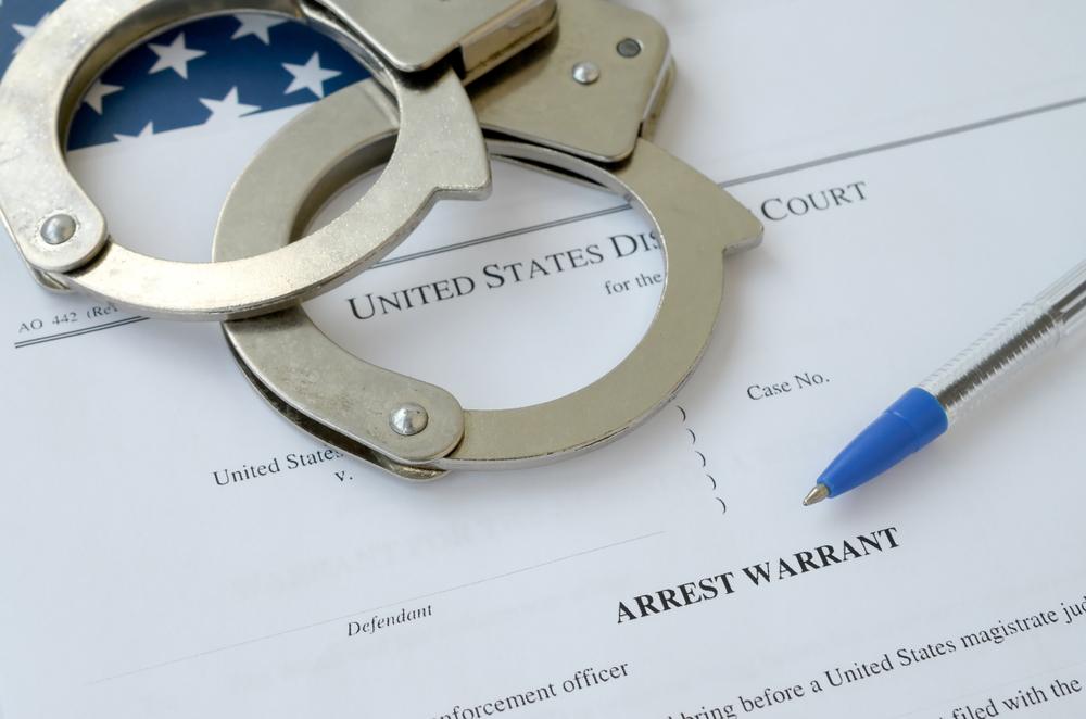 An Ohio arrest warrant document next to handcuffs. What you need to know.