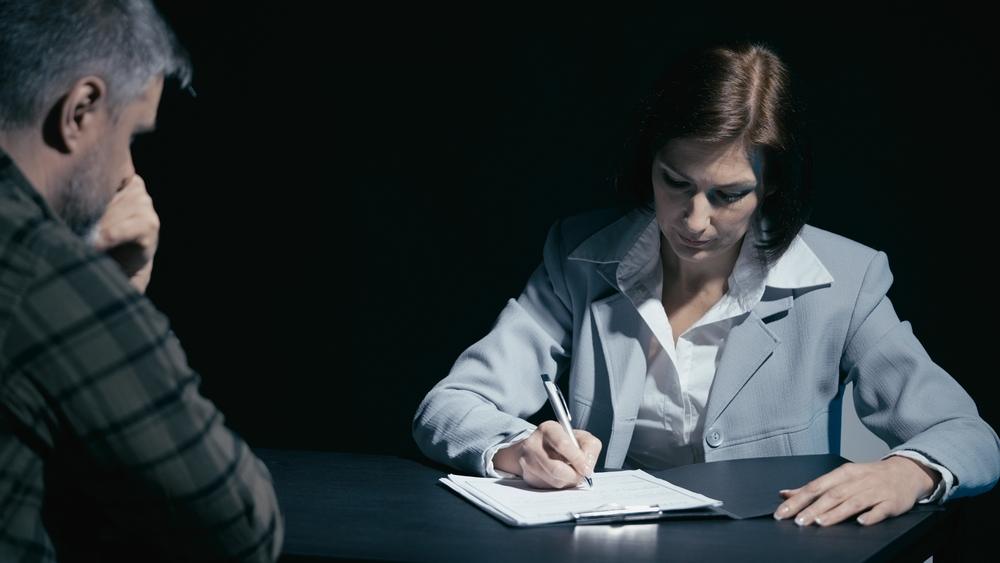 Suspected man talks to his lawyer, who is making notes in the interrogation room